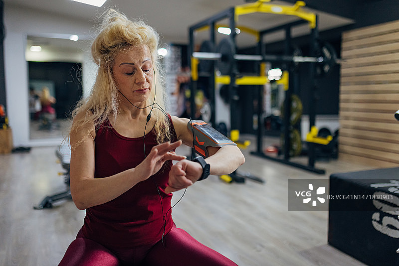 穿着运动服的严肃运动女性在开始重量训练前调整智能手表图片素材