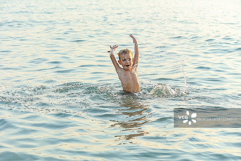 顽皮的小男孩在海里玩，溅起水花。图片素材