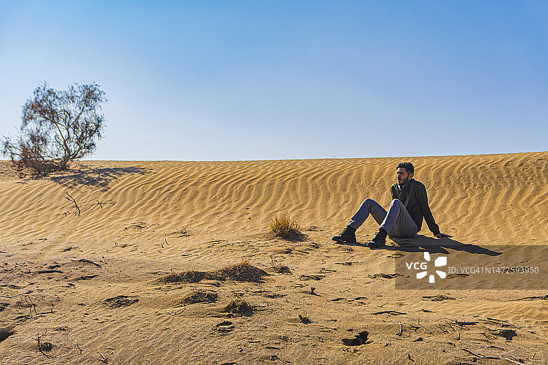 伊朗伊斯法罕省马廷阿巴德，一名男子坐在沙漠中的沙丘上，天空晴朗图片素材