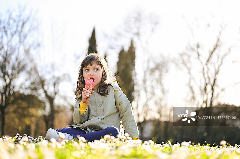 日落时分，一个学龄前女孩在阳光明媚的草地上吃冰淇淋。图片素材