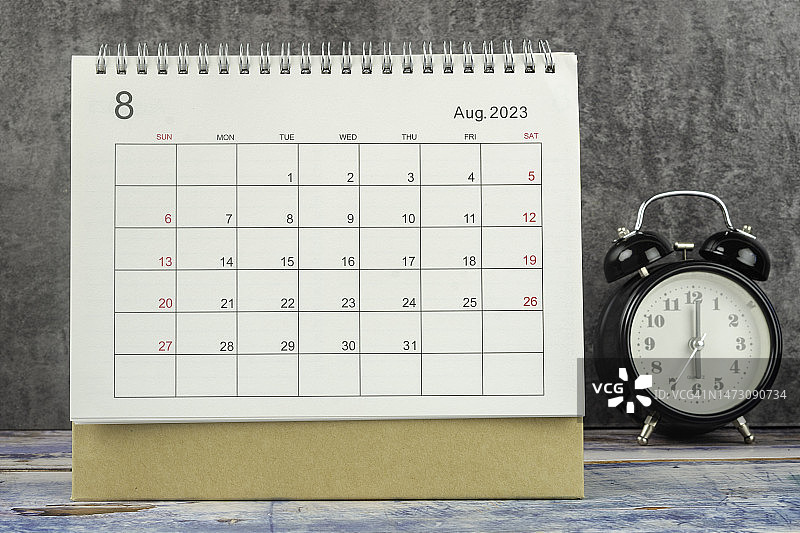 日历桌2023:八月是组织者计划和截止日期的月份，在桌子上放一个闹钟，背景是水泥。图片素材