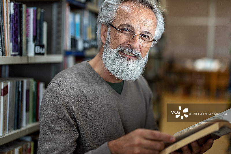 白发男子在图书馆拿着一本书对着镜头微笑图片素材