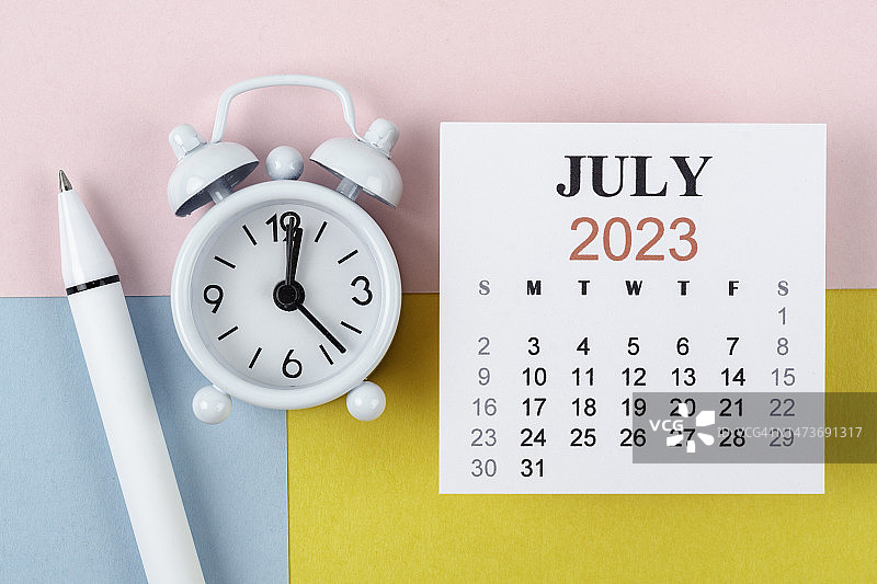 日历桌2023:7月是组织者用闹钟和白笔在双色纸背景上做计划和截止日期的月份。图片素材