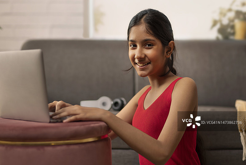 一个微笑的女孩在客厅使用笔记本电脑的肖像图片素材