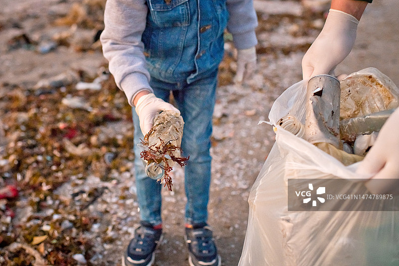 志愿者用手套和袋子收集废弃塑料垃圾，双手清洁海滩的特写镜头。环境污染与生态问题概念。图片素材
