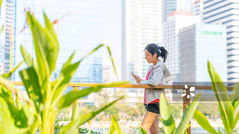 一名亚洲女子在公园慢跑时戴着耳机听音乐。图片素材