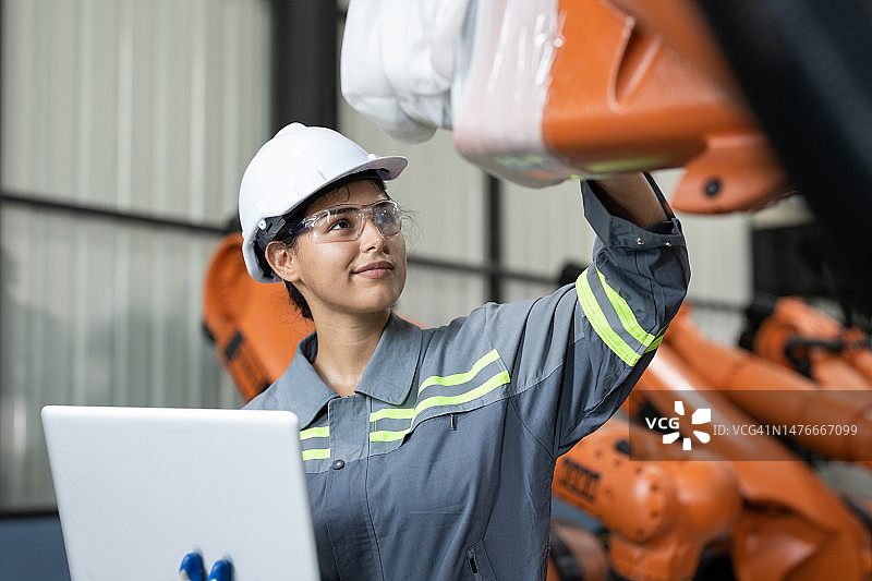 在装配机器人仓库工厂，女工程师用笔记本电脑检查新机器臂的质量图片素材