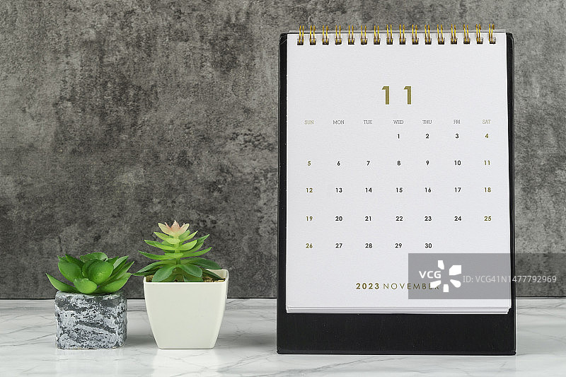 日历桌2023:11月是组织者计划和截止日期的月份，在混凝土墙背景下放置室内植物。图片素材