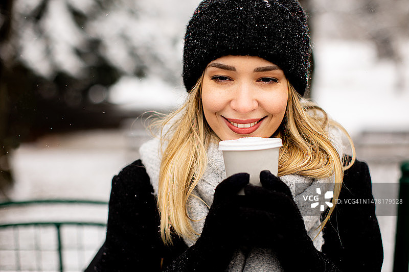 年轻女子穿着暖和的衣服，拿着外卖咖啡杯在雪中享受图片素材