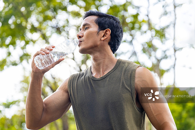 亚洲男子早上在公园慢跑时喝水。图片素材