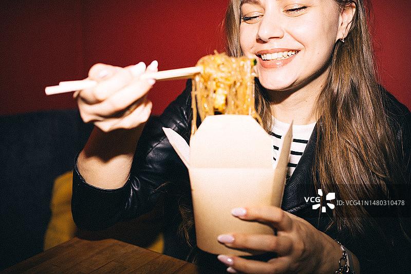 开朗的女孩吃面条，从零浪费食品纸盒和木筷子图片素材