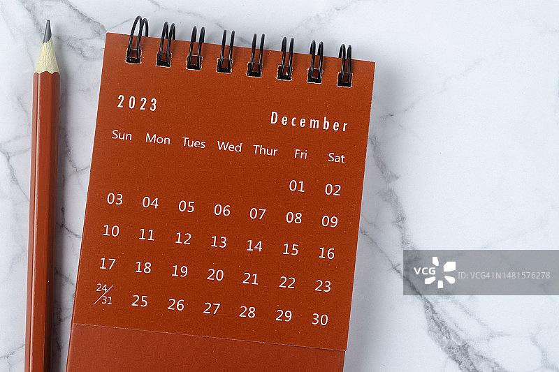 2023年日历桌面的俯视图:12月是组织者用红色铅笔在白色大理石背景上制定计划和截止日期的月份。图片素材