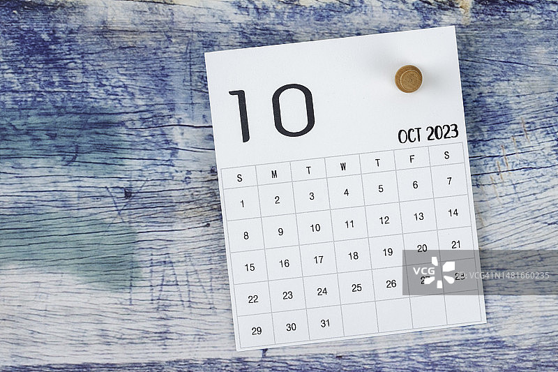 日历台2023:十月是组织者计划和最后期限的月份，蓝色木制背景上有一个图钉。图片素材