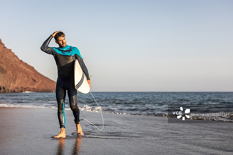一个冲浪者走在沙滩上，手里拿着冲浪板图片素材