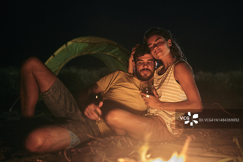 一对相爱的夫妇在海滩露营之夜喝酒。图片素材