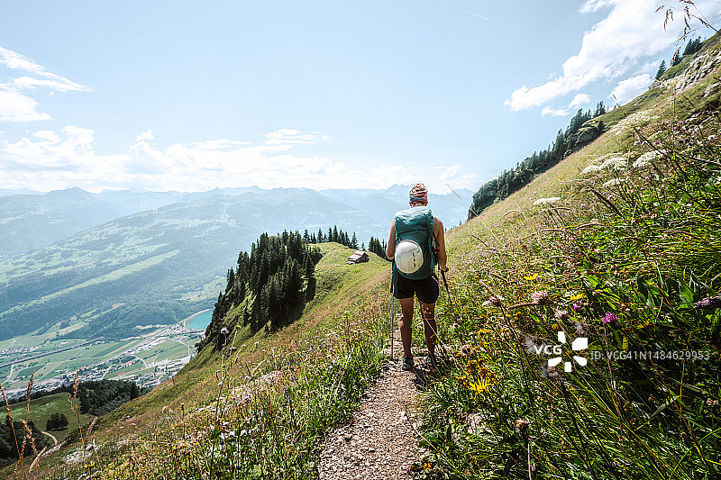 运动女子徒步在陡峭的草地上的花径与风景秀丽的瓦伦泽湖和瑞士阿尔卑斯山。瑞士，瓦伦塞，圣加仑，瑞士，欧洲。图片素材