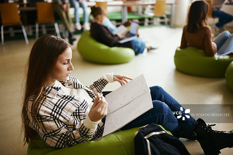 放松的女学生在校园里从笔记本上阅读。图片素材