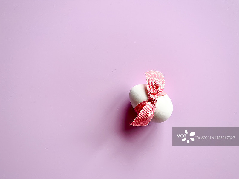 白色鸡蛋的特写，粉红色的背景上有粉红色的丝带图片素材