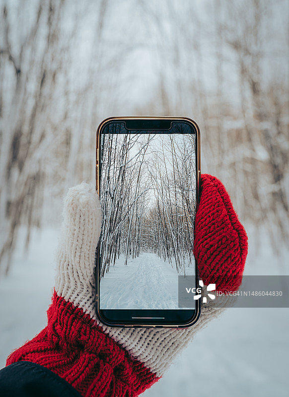 戴着连指手套的手拿着手机的特写，手机上有冬天的照片图片素材