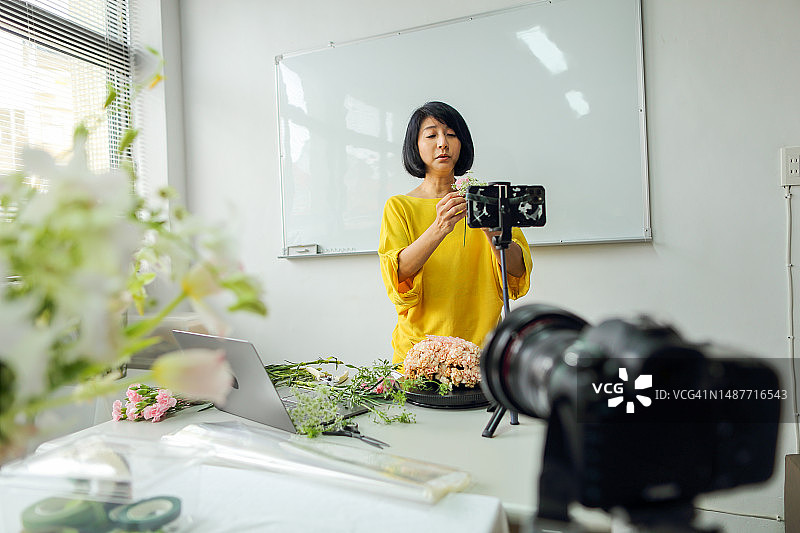 亚洲女花艺老师，小型企业花艺课程的老板，在线教授插花课程，使用智能手机，相机和笔记本电脑进行视频记录。电子学习，在线教程的概念图片素材