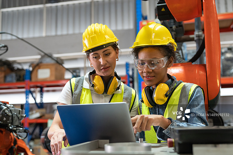 女自动化工程师身穿安全背心，头戴黄色头盔，使用笔记本电脑检查工业工厂新型焊接机械臂机图片素材