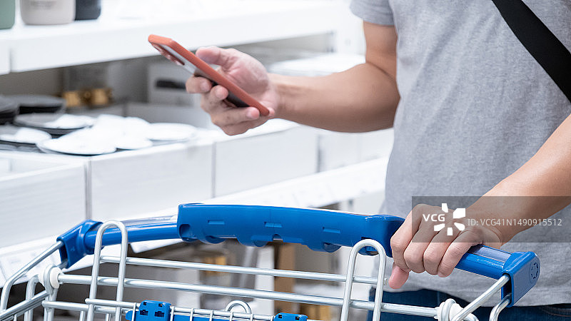 在杂货店或超市，顾客用智能手机手持购物车。图片素材
