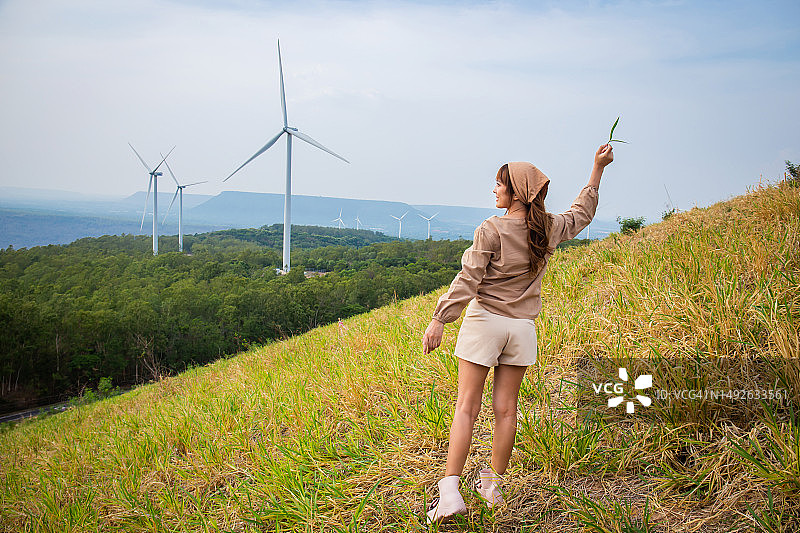 一个穿着可爱裙子的女人站在草地上，背景是风车和山脉。旅行自由概念图片素材