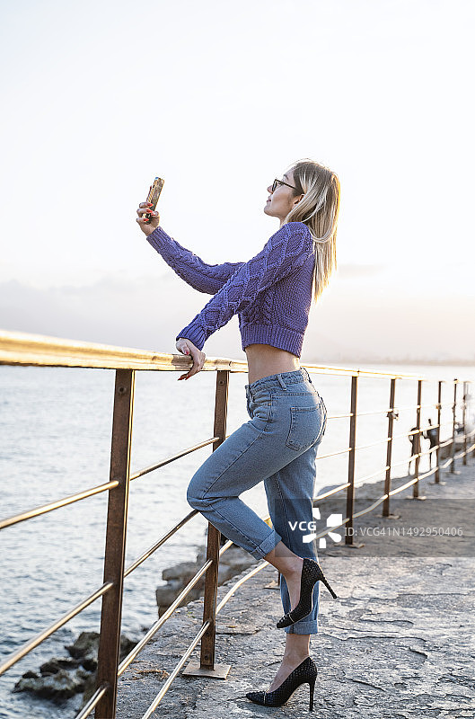 在土耳其安塔利亚的码头上，年轻的美女用智能手机摆姿势拍照图片素材