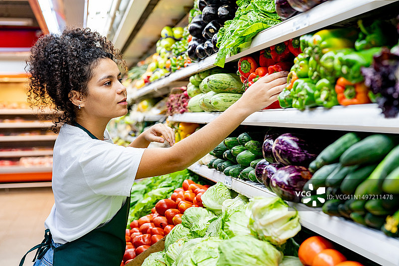 拉丁美洲的女售货员在超市的冷藏区整理甜椒图片素材
