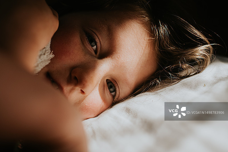 一个小女孩躺在白色的枕头上，看着镜头的特写图片素材