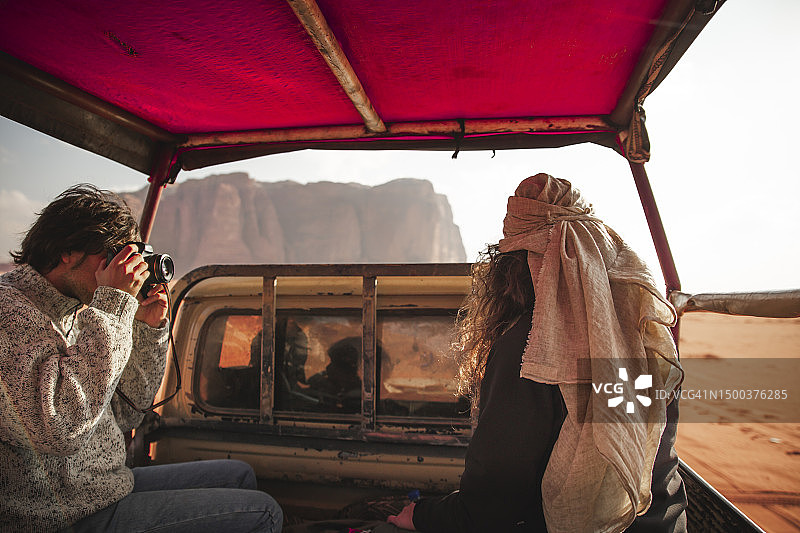 在一次沙漠旅行中，一个男人在车里用相机给一个女人拍照图片素材