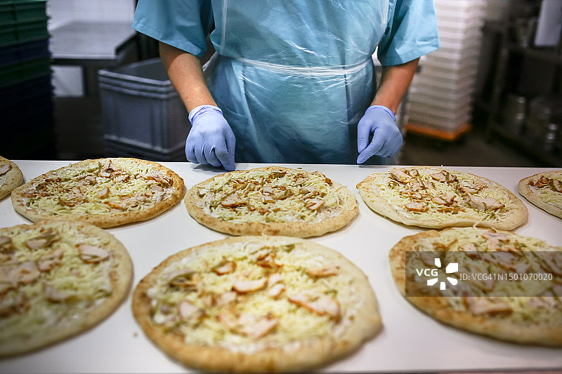 工人在输送带上控制披萨生产过程的手图片素材