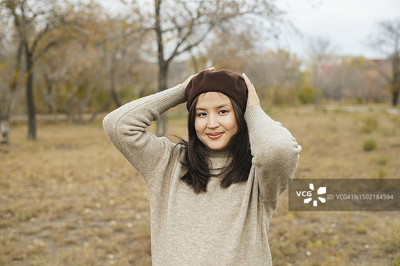 秋天，穿着米色毛衣和棕色贝雷帽的年轻亚洲妇女在户外的肖像图片素材