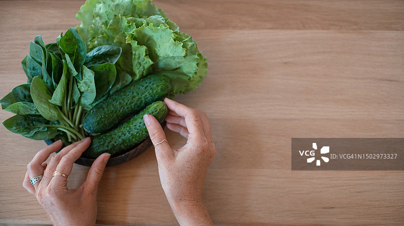 女人的手摸的是黄瓜、生菜和菠菜组成的绿色健康蔬菜。图片素材