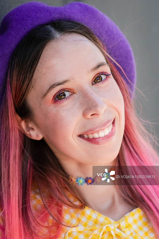 一个迷人的微笑的年轻女孩的肖像，戴着紫色的贝雷帽，粉红色的头发图片素材