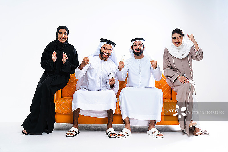 美丽的阿拉伯中东朋友，穿着传统的酋长国服装，坐在白色背景下的橙色沙发上图片素材