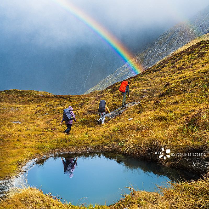 徒步旅行者以彩虹为背景爬山。图片素材