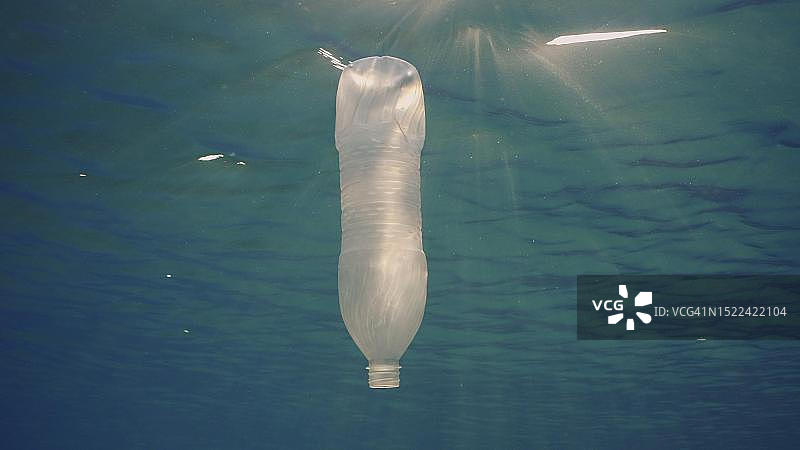 一次性塑料瓶在明亮的阳光下漂浮在水面下。一个塑料瓶被扔进海里，在清晨的阳光中慢慢地漂浮在水柱中，埃及红海图片素材