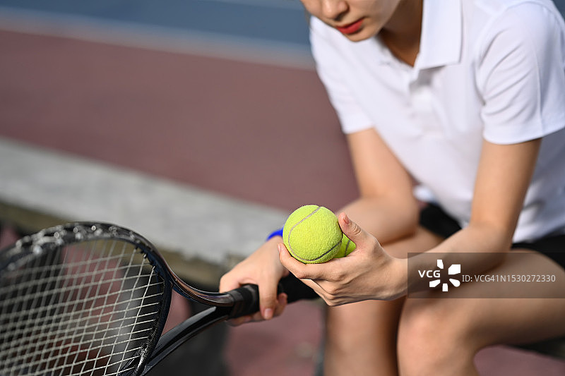 漂亮的年轻女运动员拿着球拍坐在网球场的长凳上。图片素材