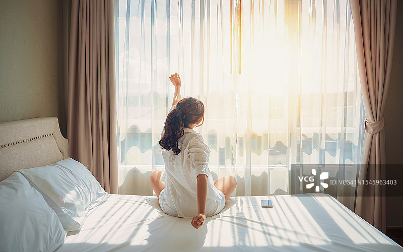 亚洲女性在家里起床伸展身体，在卧室里放松。清晨出门，醒来休息阳光明媚的一天。生活方式的概念图片素材