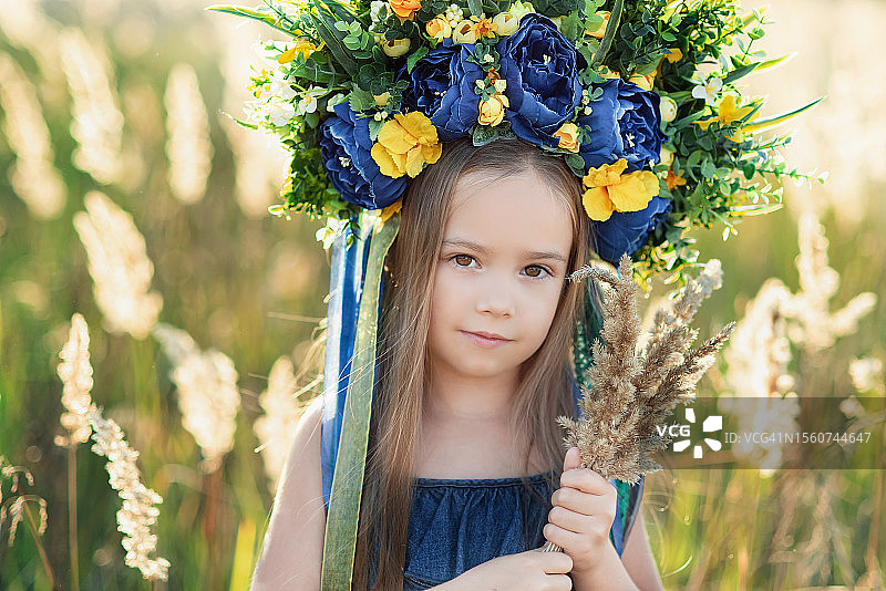 乌克兰小女孩的肖像，穿着蓝色衬衫，戴着蓝黄相间的花圈，黄蓝相间的丝带，手里拿着一把狗尾草图片素材