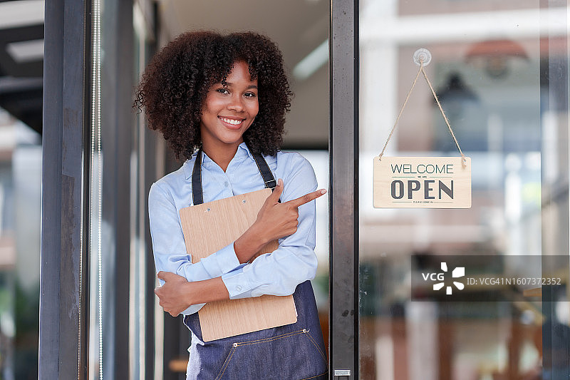 餐馆、咖啡馆或酒吧的女店主或员工，带着欢迎的微笑，展示“开放”标志。图片素材