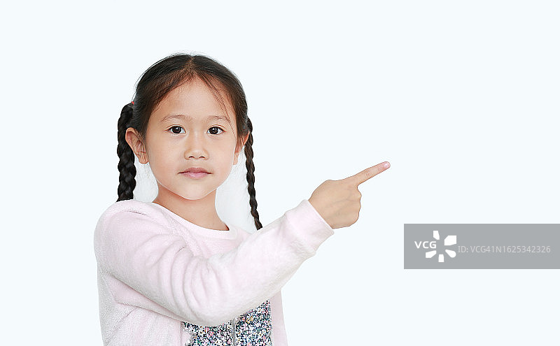 开朗的小女孩用食指指着旁边，用空白的白色背景呈现出孤立的东西。教育观念中的亚洲女学生。图片素材