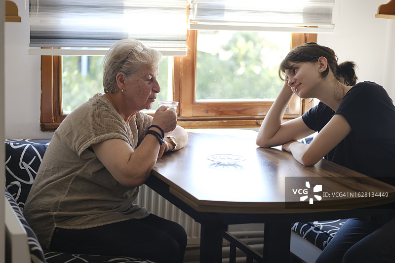 奶奶和孙女在厨房的桌子边喝茶聊天图片素材