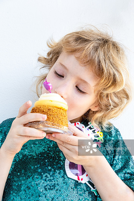 漂亮的小生日女孩咬着她的庆祝蛋糕。图片素材