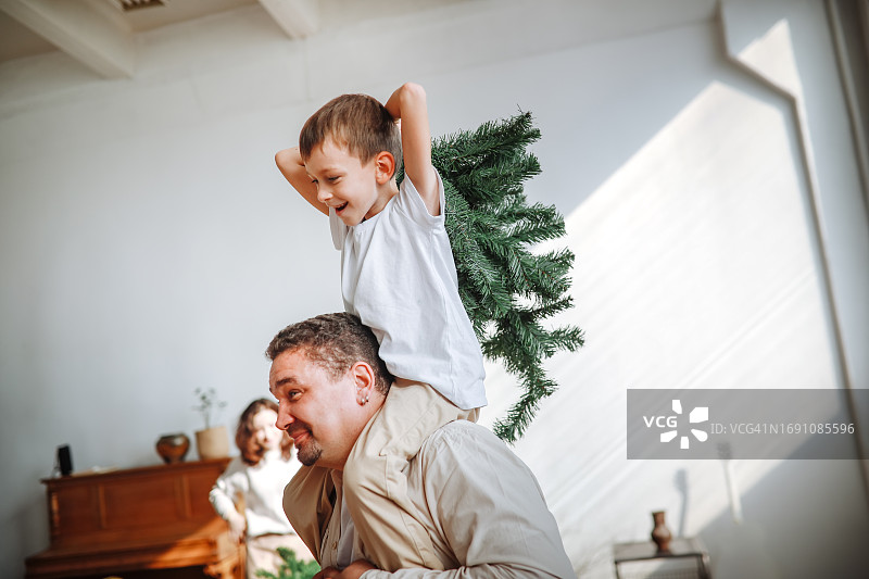 爸爸背着儿子在家里装饰圣诞树，搞笑的全家福图片素材