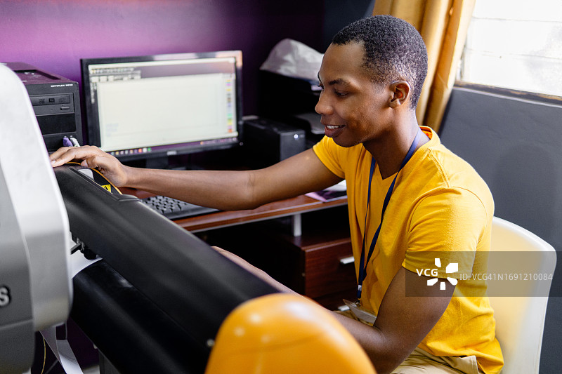 一位年轻的非洲男子平面设计师使用绘图仪切割图片素材