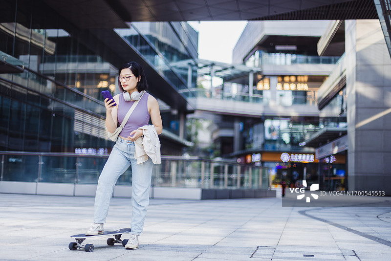 亚洲女子在城市里边玩手机边滑冰图片素材