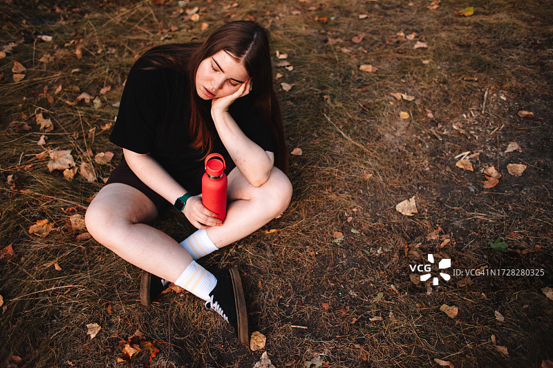 秋天，年轻女子在森林里锻炼后，拿着可重复使用的水瓶放松图片素材