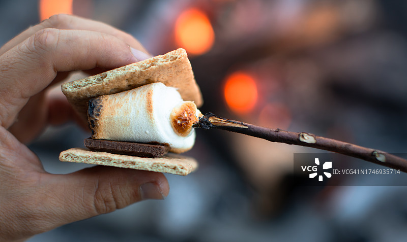 一个人在篝火旁烤棉花糖，享受着s'more的特写。露营的概念。图片素材
